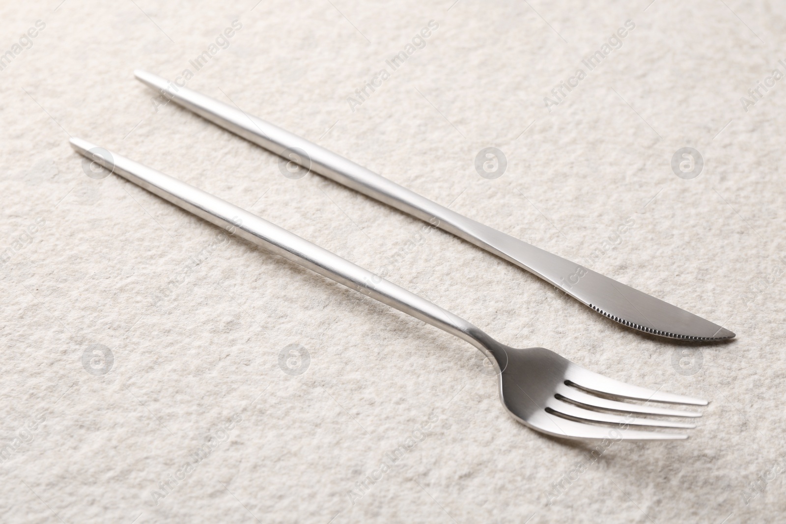 Photo of Stylish cutlery. Silver knife and fork on light textured table