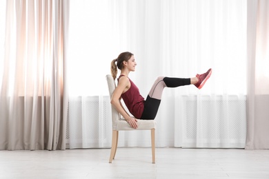 Photo of Young woman exercising with chair indoors. Home fitness