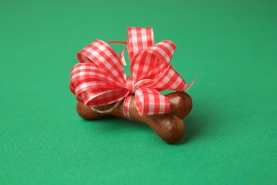 Photo of Bone shaped dog cookie with red bow on green background, closeup