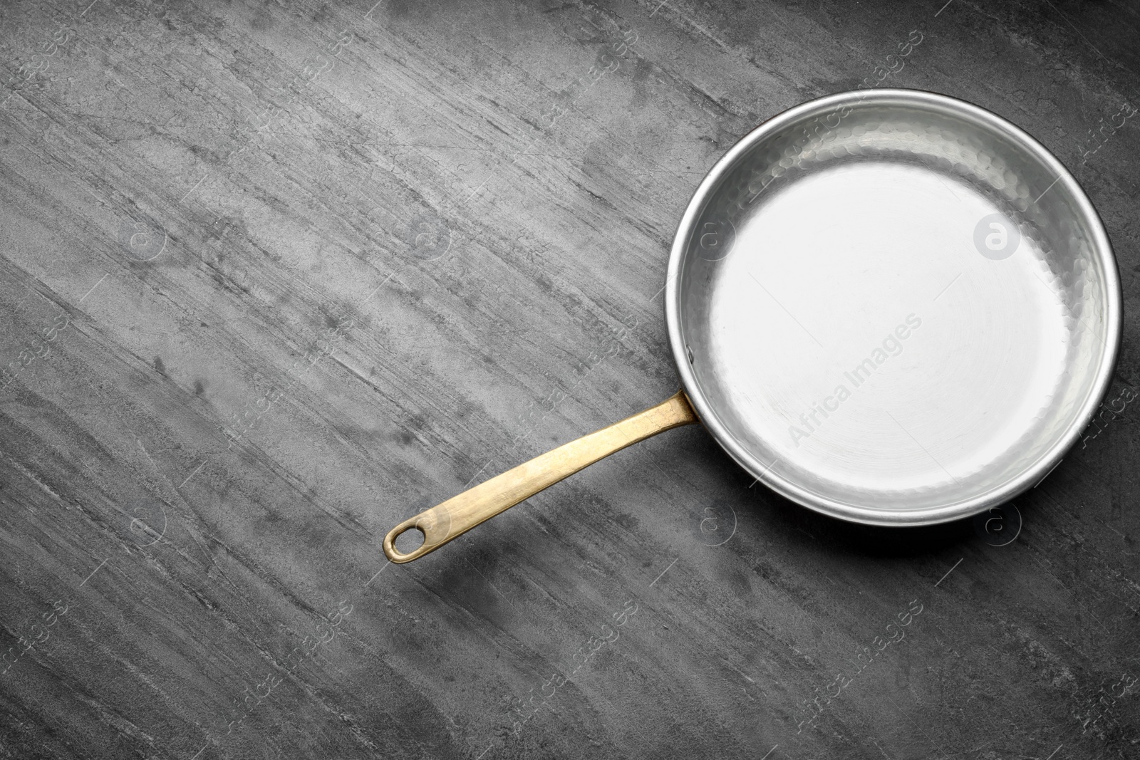 Photo of New metal frying pan on grey table, top view. Space for text