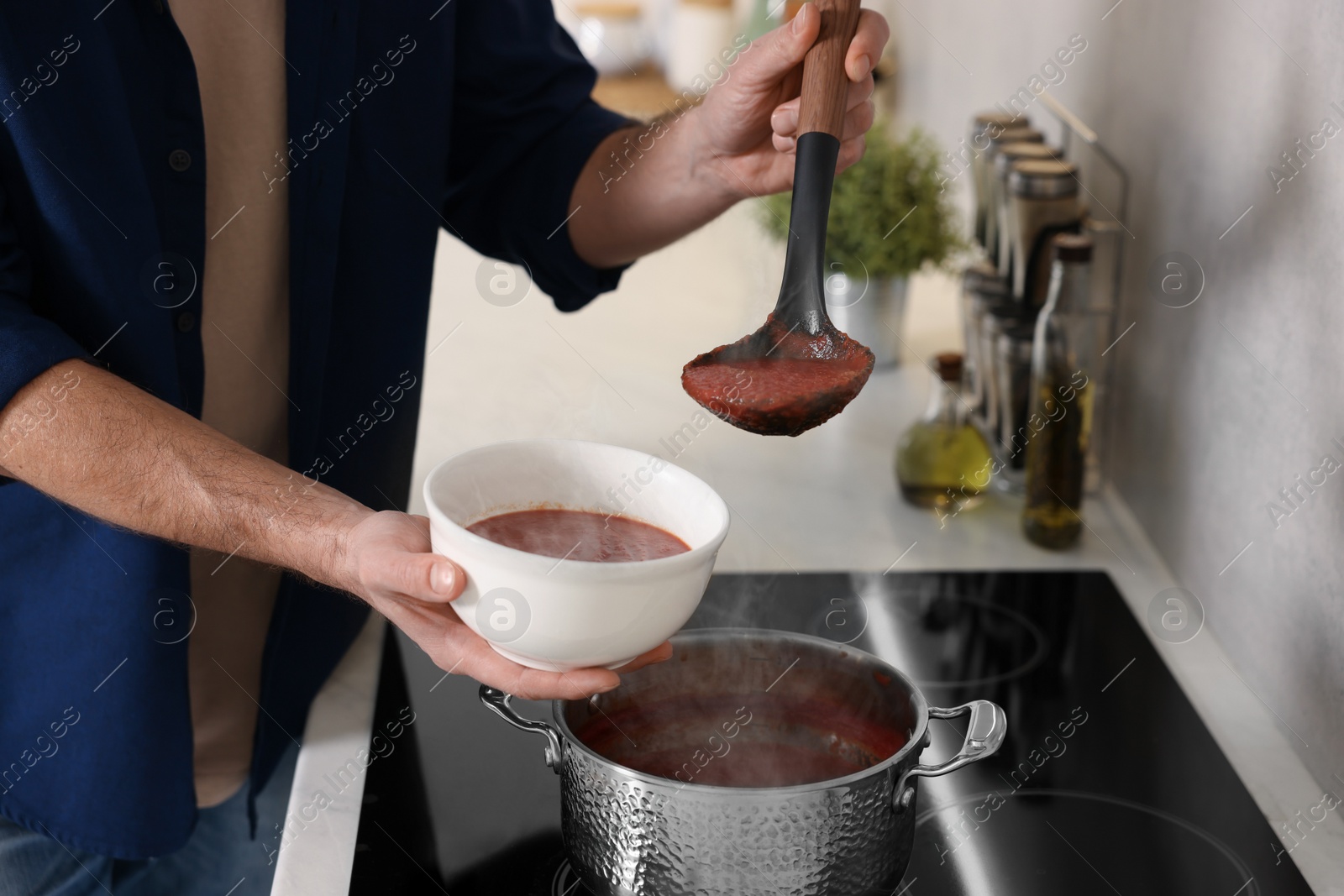 Photo of Man pouring delicious tomato soup into bowl in kitchen, closeup