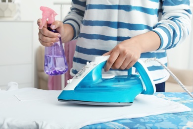 Woman ironing clothes on board indoors, closeup