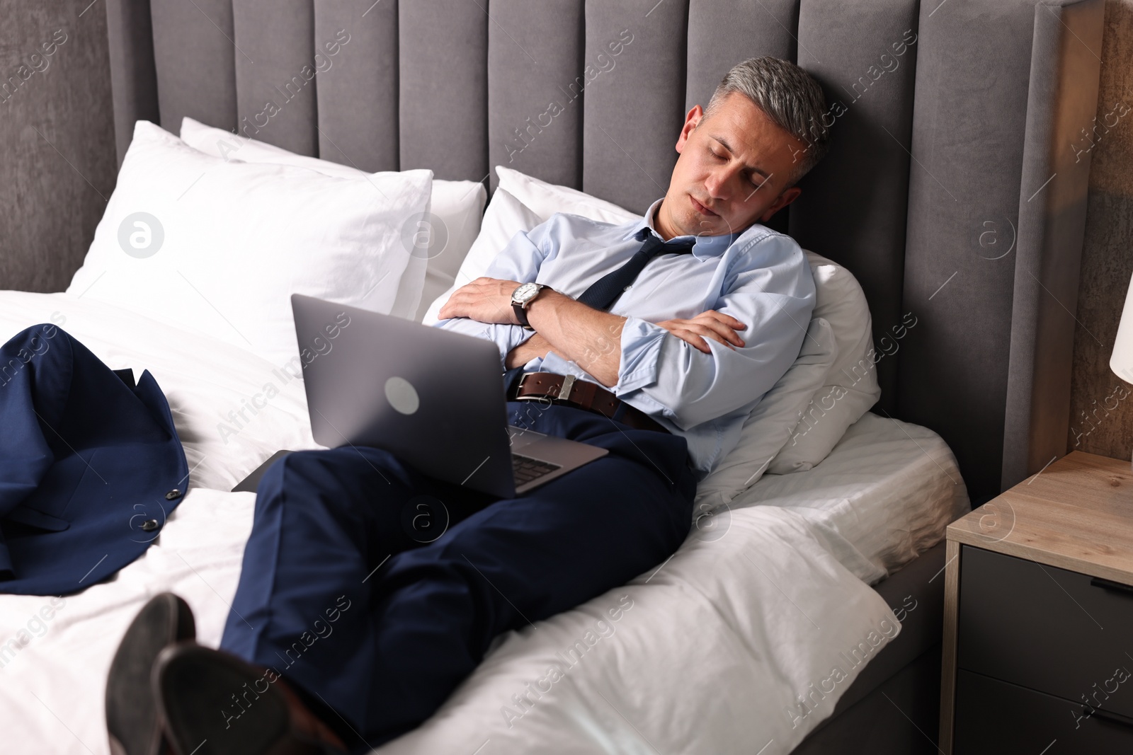 Photo of Businessman with laptop sleeping on bed indoors