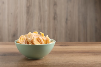 Photo of Delicious dried jackfruit slices in bowl on wooden table. Space for text