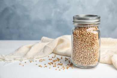 Photo of Jar with green buckwheat on white table. Space for text