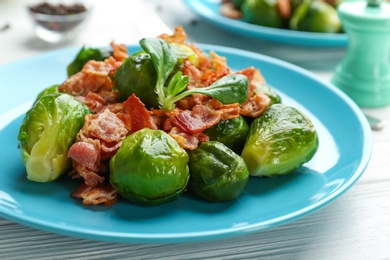 Photo of Tasty roasted Brussels sprouts with bacon on white wooden table, closeup