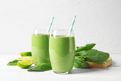 Photo of Glasses of healthy green smoothie with fresh spinach on white wooden table against light background