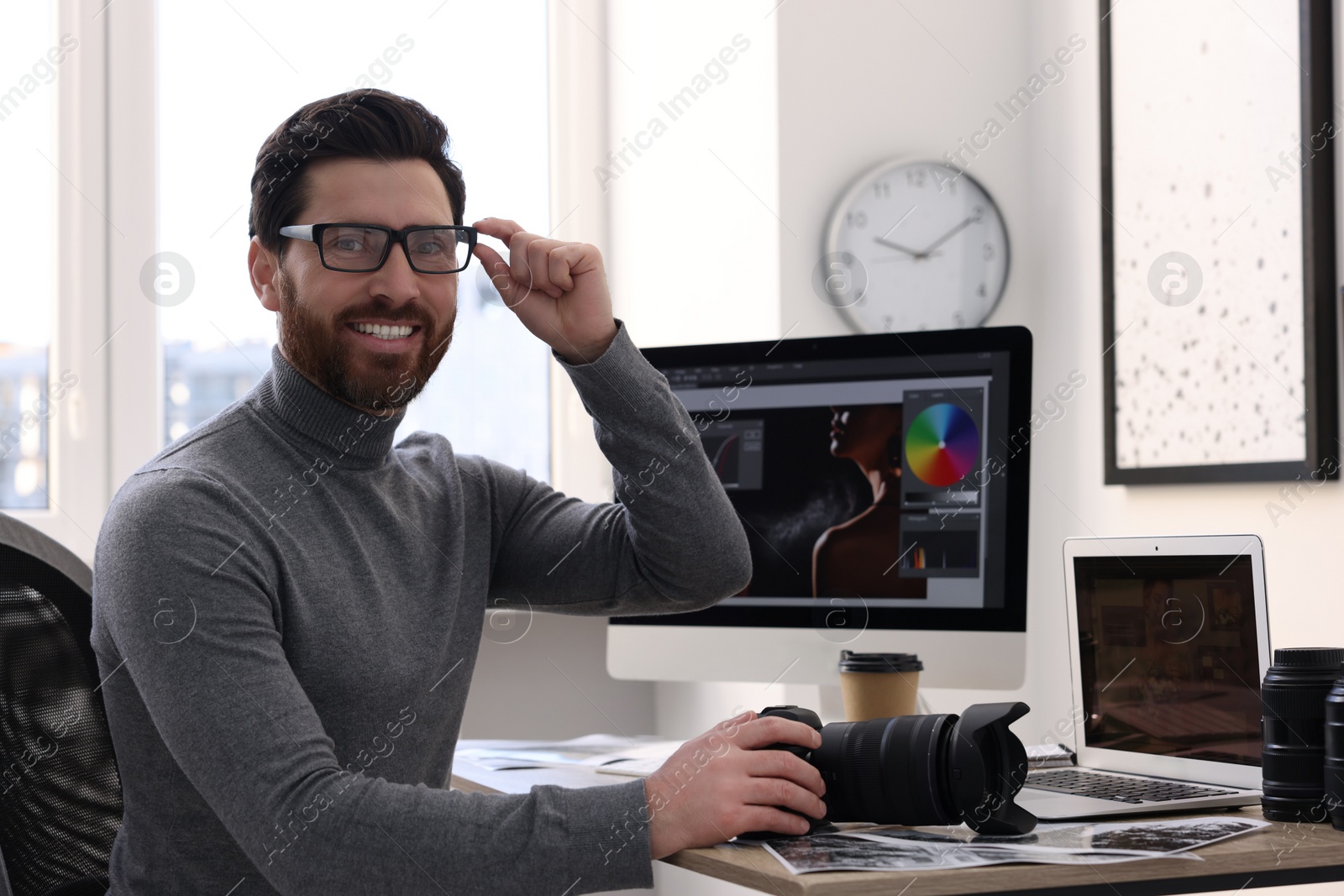 Photo of Professional photographer in glasses holding digital camera at table in office