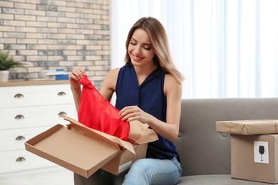 Photo of Young woman opening parcel on sofa in living room