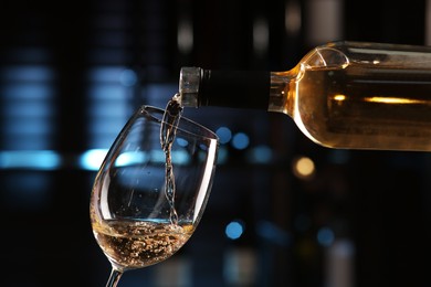 Photo of Pouring white wine from bottle into glass on blurred background, closeup