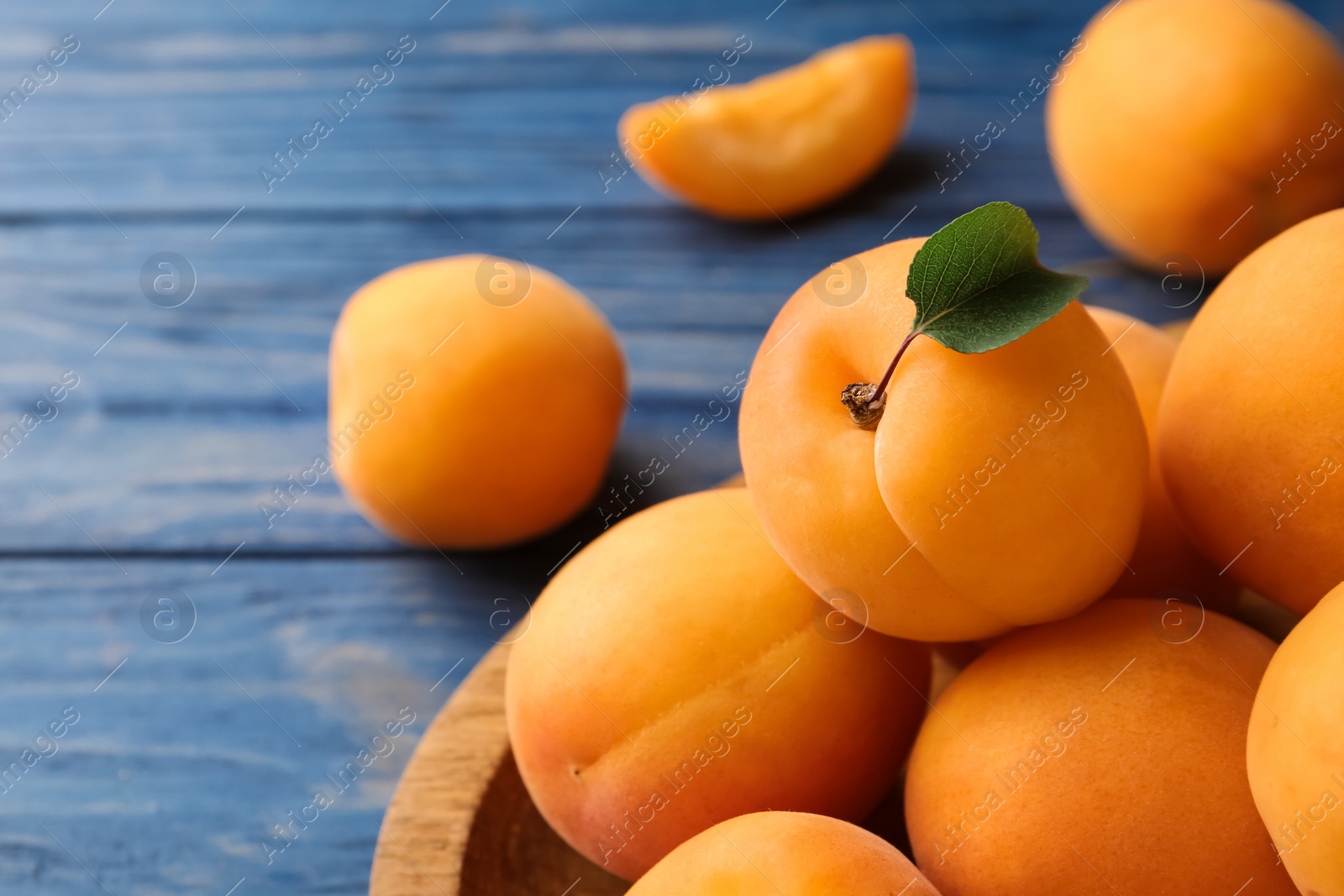 Photo of Plate of delicious apricots on blue wooden background, closeup. Space for text