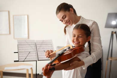 Photo of Young woman teaching little girl to play violin indoors