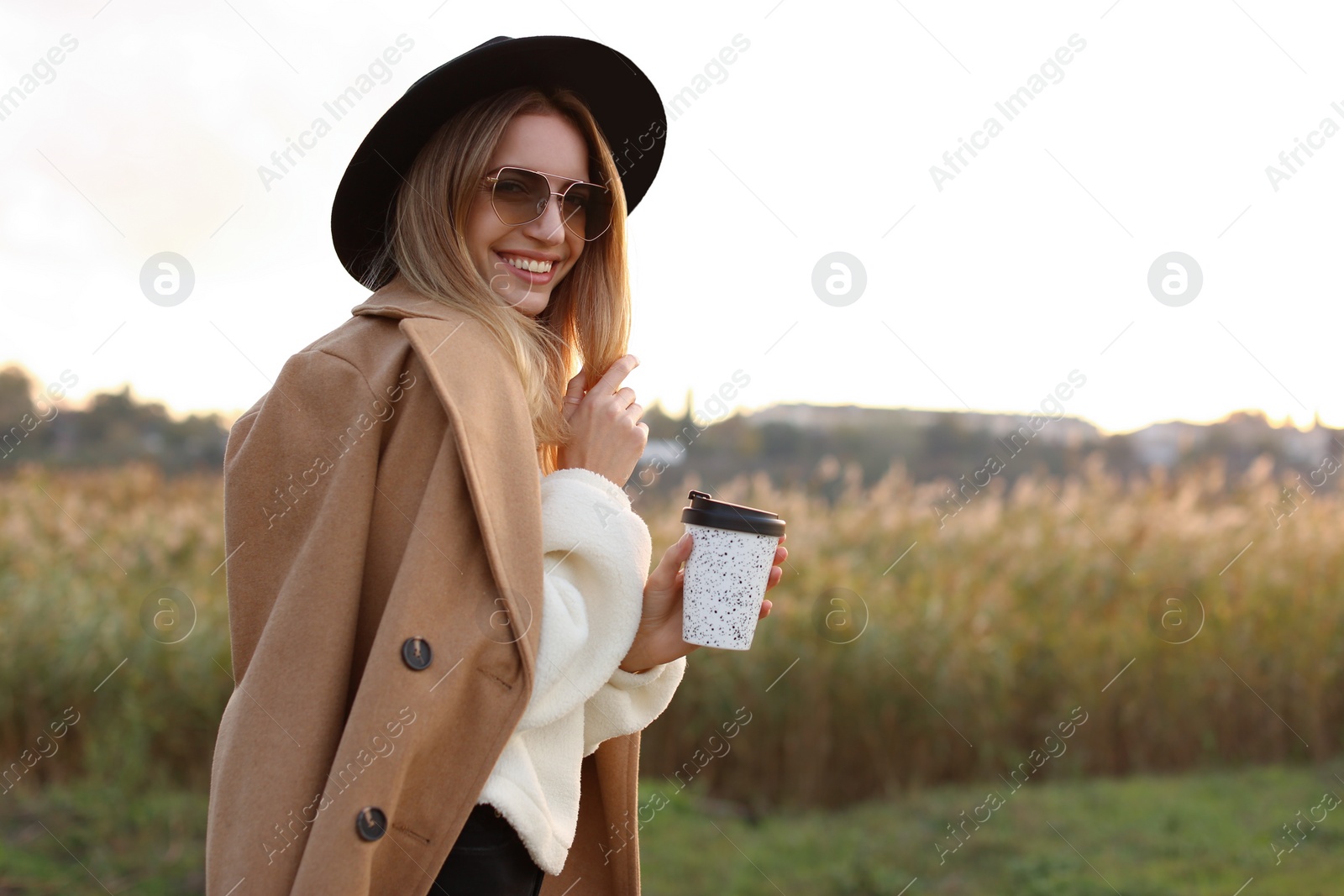 Photo of Beautiful young woman with cup of coffee wearing stylish autumn clothes outdoors