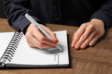 Woman writing in notebook at wooden table, closeup