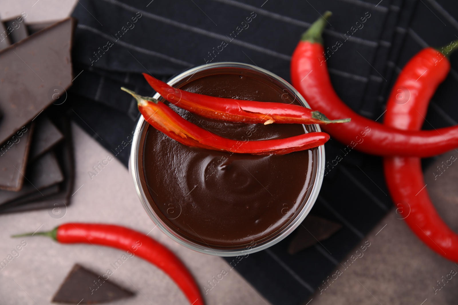 Photo of Delicious hot chocolate with chili peppers on brown textured table, flat lay