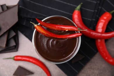 Delicious hot chocolate with chili peppers on brown textured table, flat lay