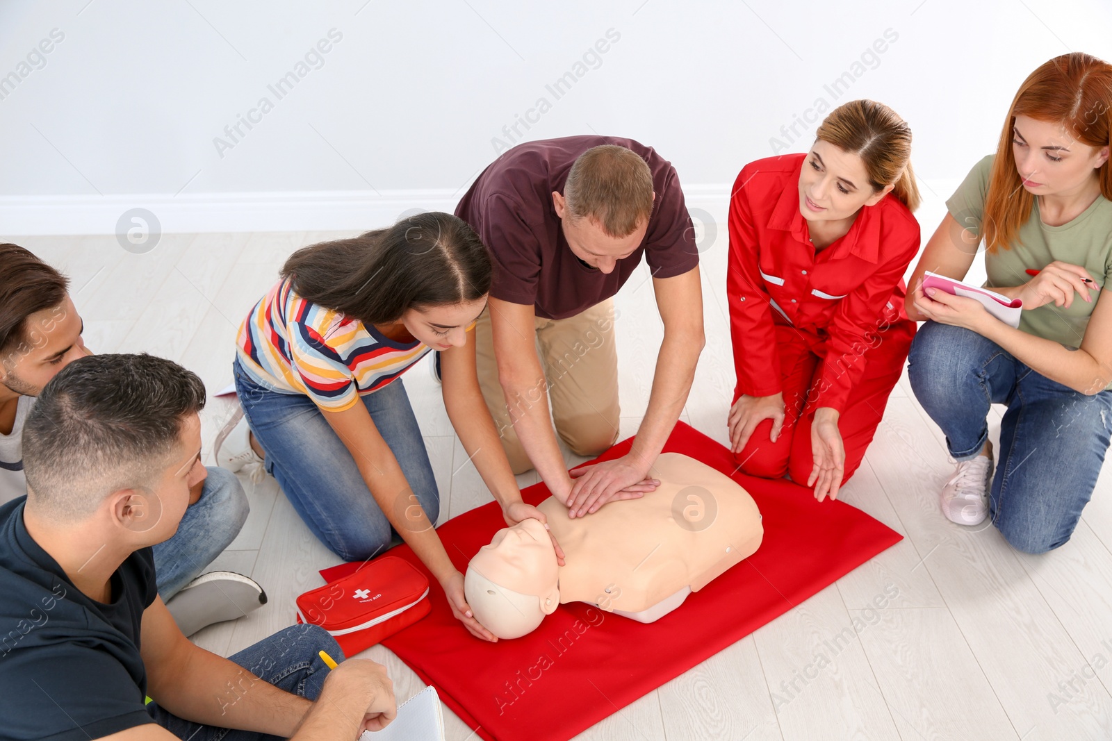 Photo of Group of people with instructor practicing CPR on mannequin at first aid class indoors