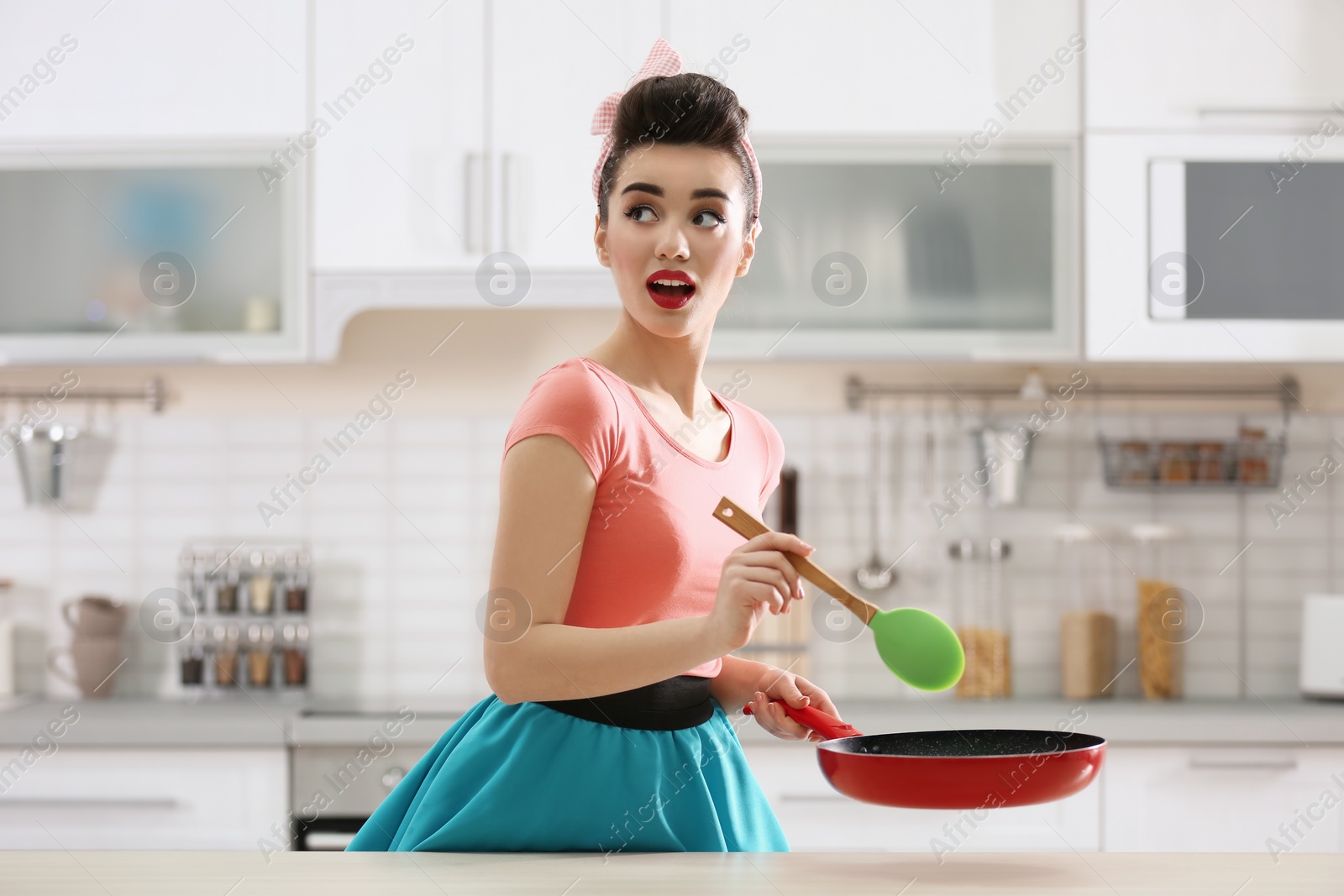 Photo of Funny young housewife with spoon and frying pan in kitchen