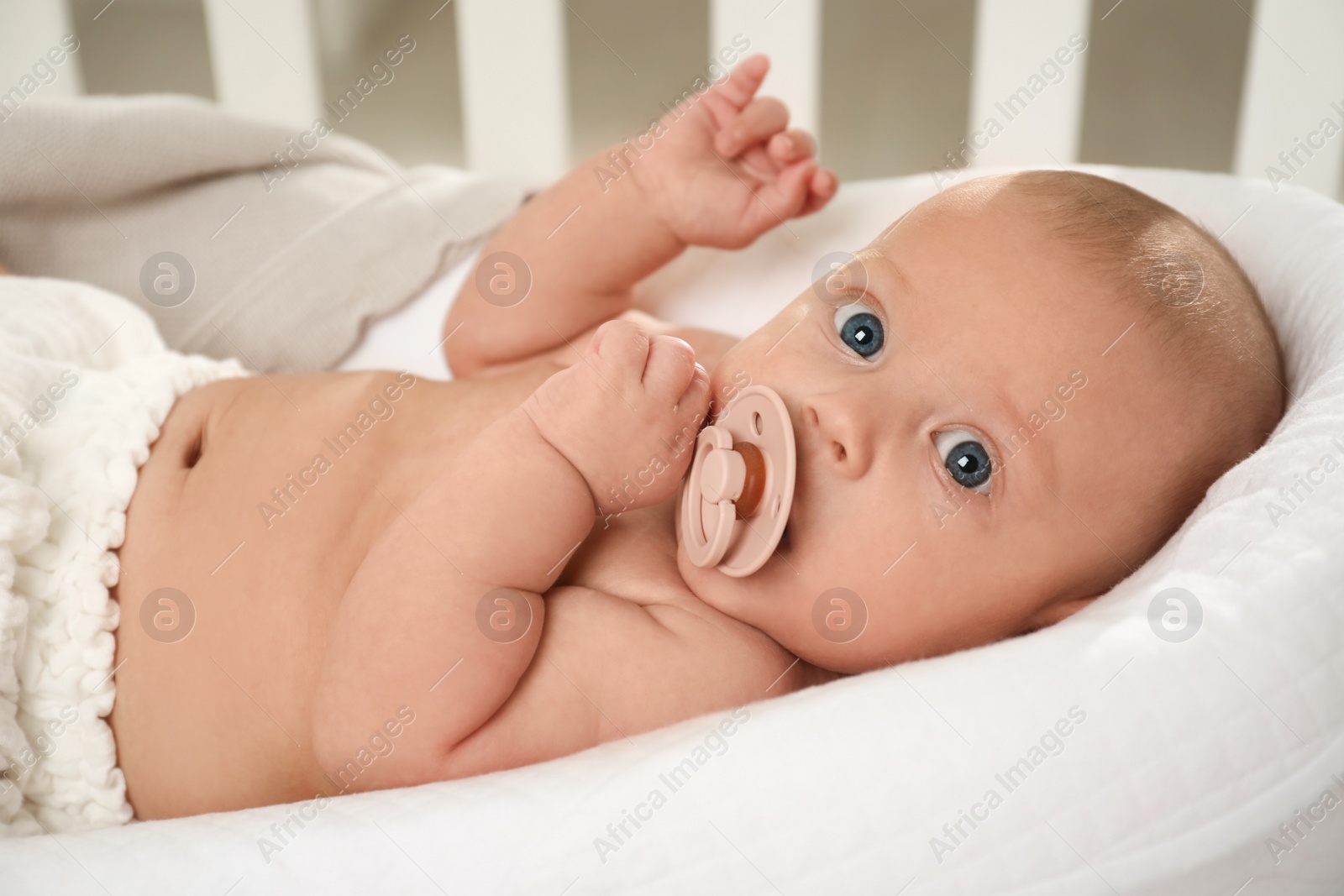 Photo of Cute little baby with pacifier lying in crib