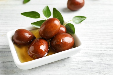 Photo of Sauce boat with jojoba oil and seeds on white wooden table