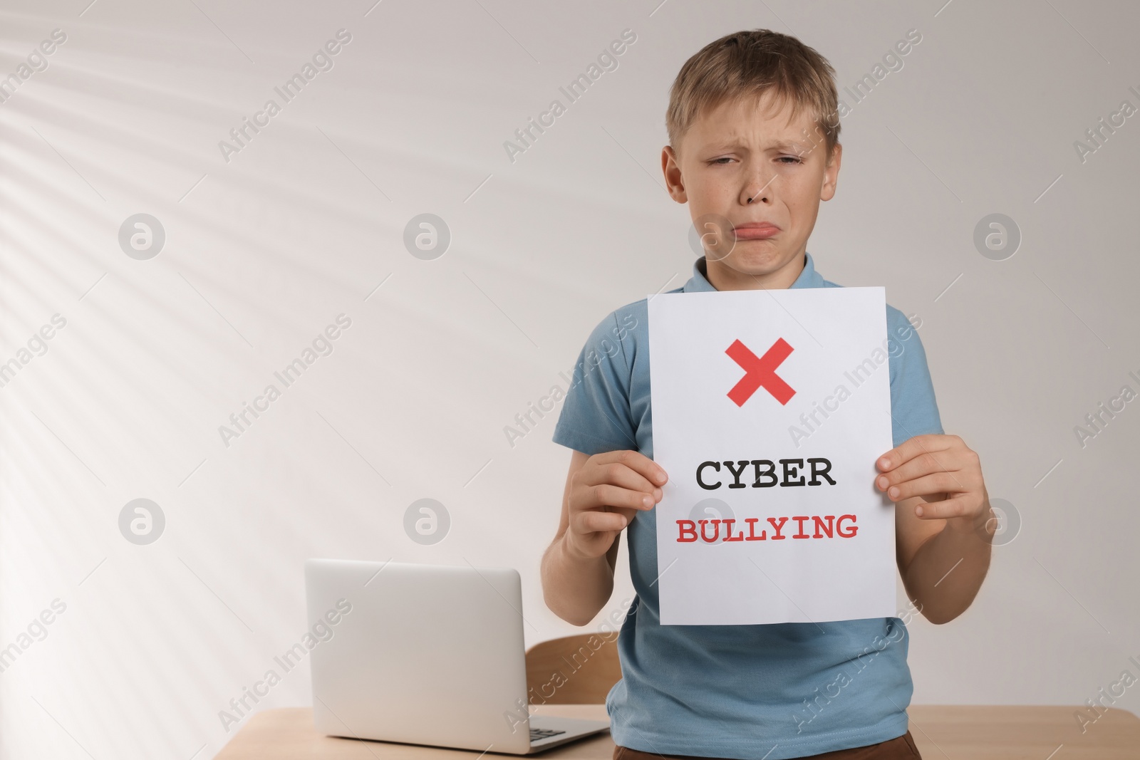 Photo of Upset holding sign with phrase Cyber Bullying near table indoors, space for text