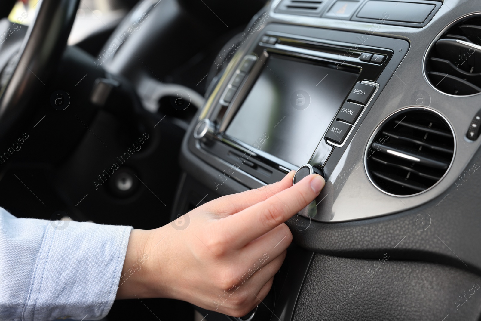 Photo of Listening to radio while driving. Woman turning volume button on vehicle audio in car, closeup