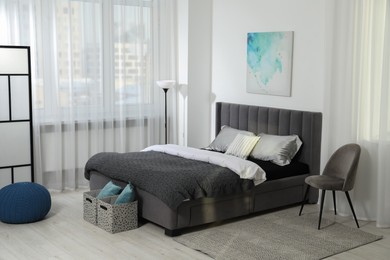 Stylish bedroom interior with large bed, pouf, lamp and chair