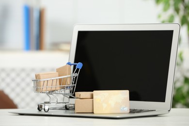Photo of Online payment concept. Small shopping cart with bank card, boxes and laptop on white table