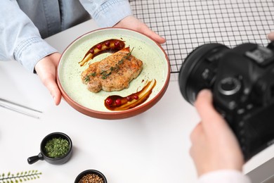 Photo of Food stylist holding plate with delicious meat medallion while photographer taking photo in studio, closeup