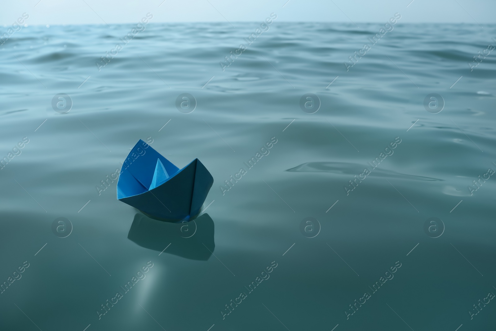 Photo of Light blue paper boat floating on water surface, space for text