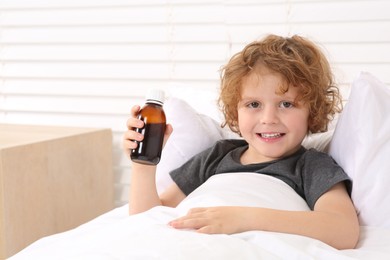 Photo of Cute boy holding bottle with cough syrup in bed. Effective medicine