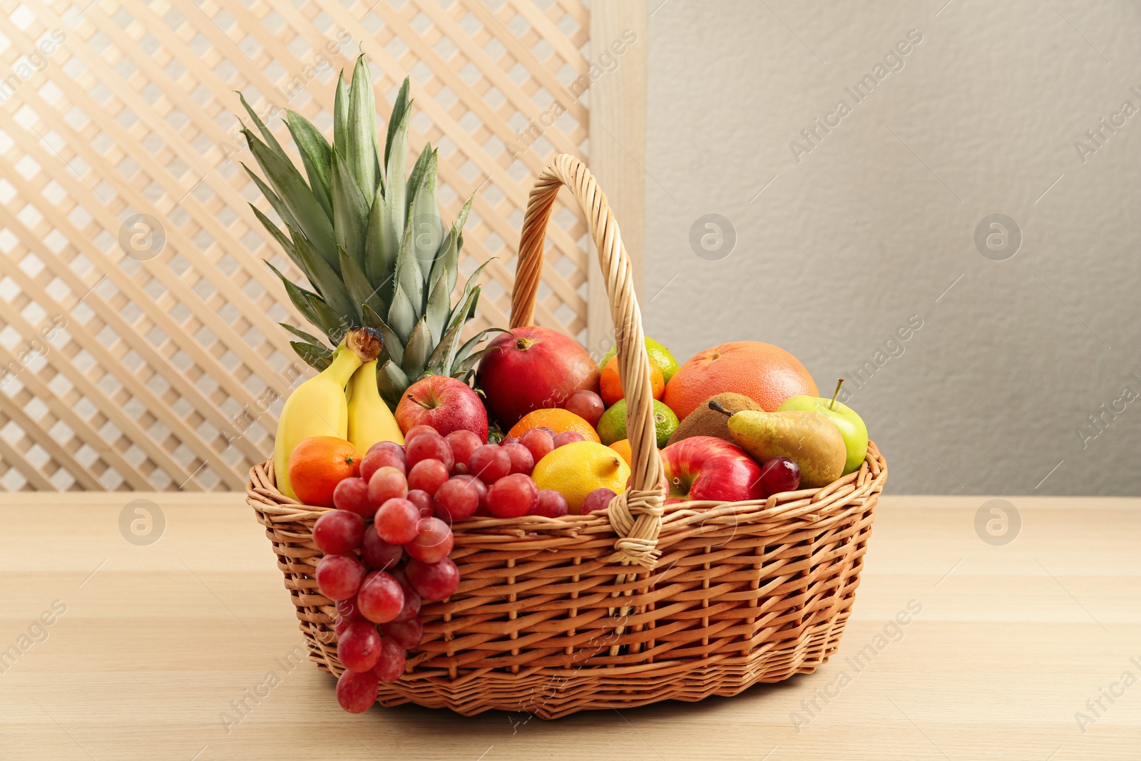 Photo of Wicker basket with different fresh fruits on wooden table