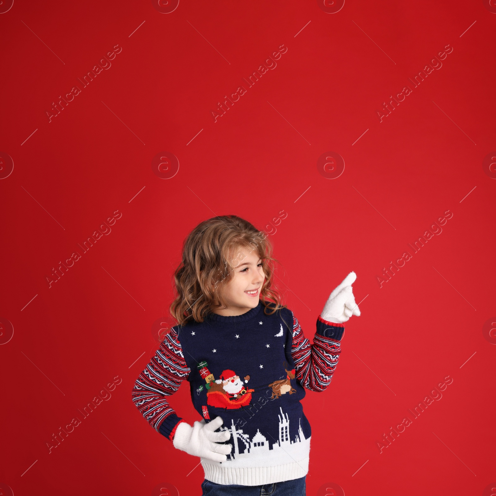 Photo of Cute little girl in Christmas sweater pointing against red background