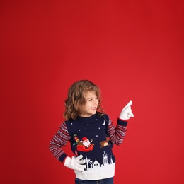 Cute little girl in Christmas sweater pointing against red background