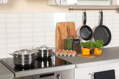 Photo of Set of clean cookware, utensils and products on table in modern kitchen