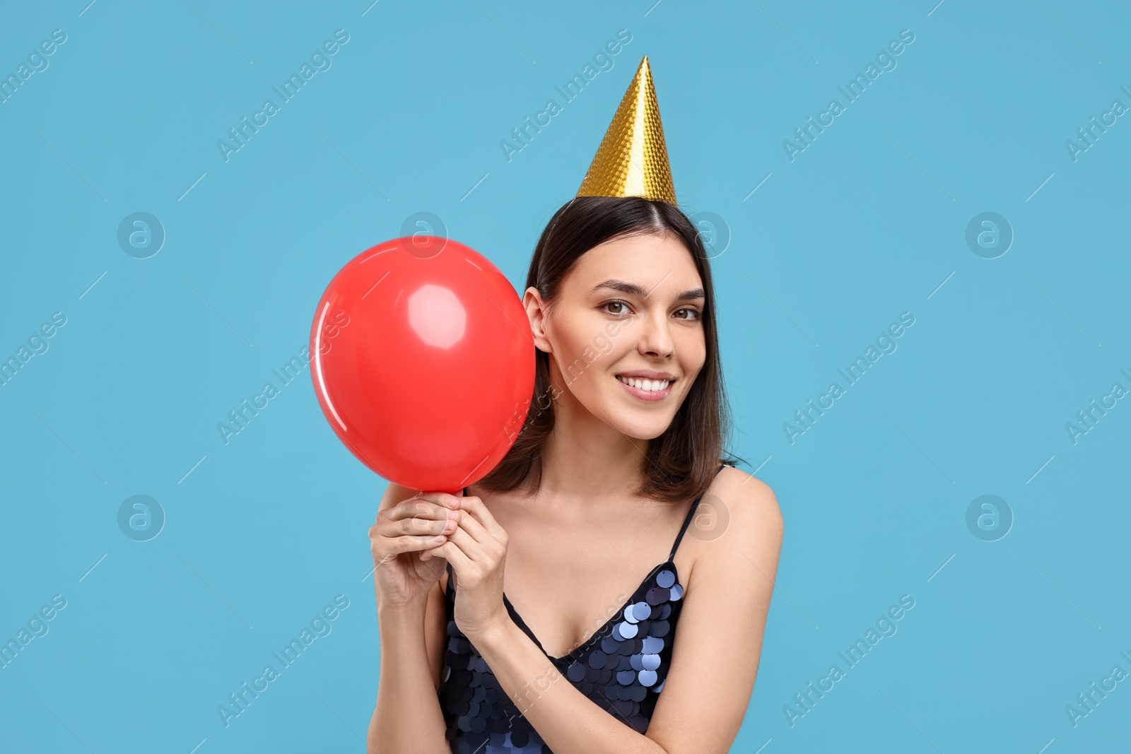 Photo of Happy young woman in party hat with balloon on light blue background