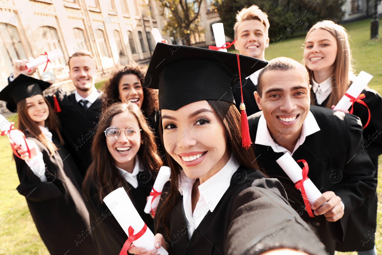 Photo of Happy students with diplomas taking selfie outdoors. Graduation ceremony