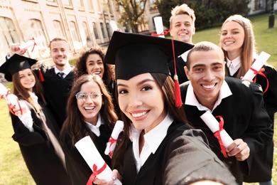 Photo of Happy students with diplomas taking selfie outdoors. Graduation ceremony
