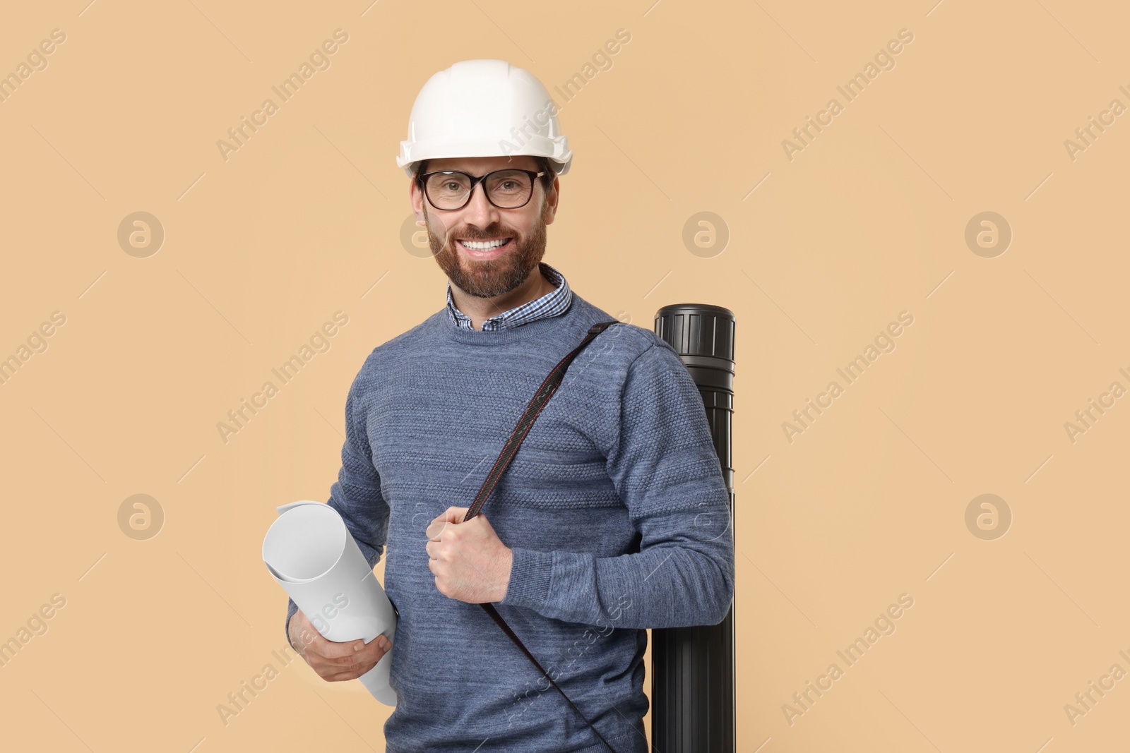 Photo of Architect in hard hat with drawing tube and draft on beige background