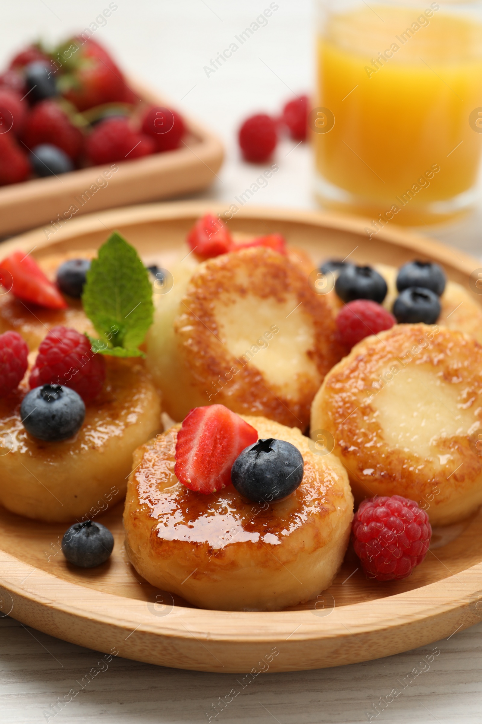 Photo of Delicious cottage cheese pancakes with fresh berries and honey on white wooden table, closeup