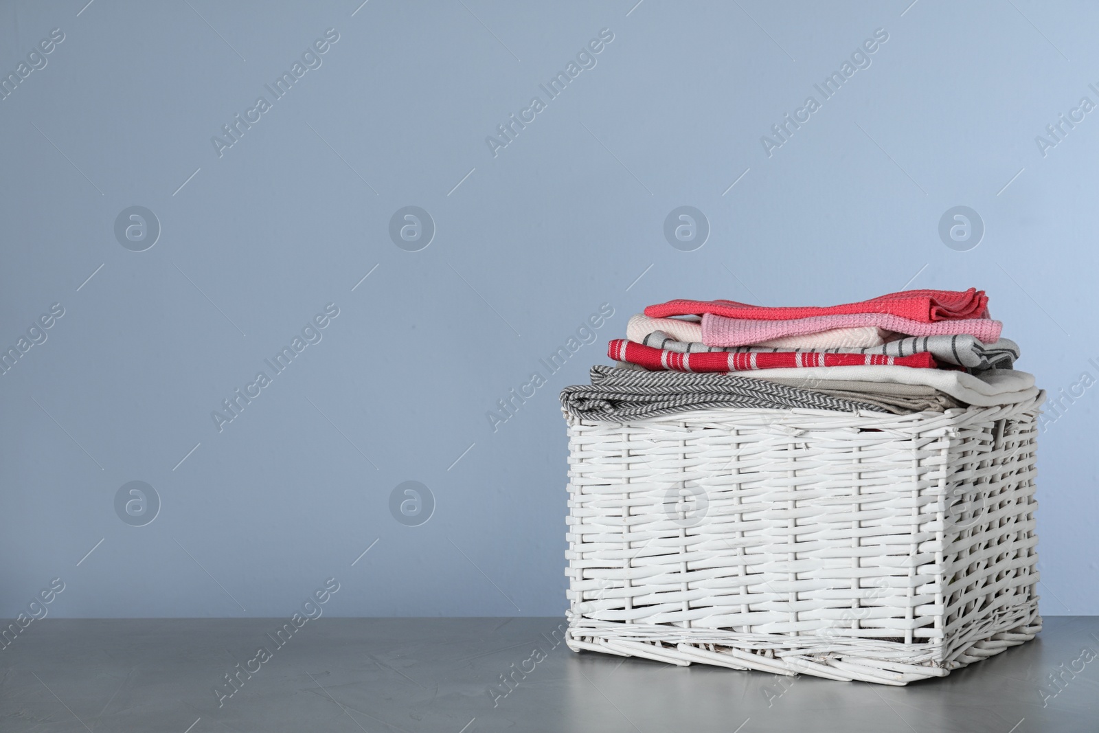 Photo of Wicker laundry basket with clean towels on table against color background. Space for text