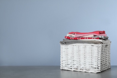 Photo of Wicker laundry basket with clean towels on table against color background. Space for text