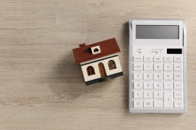 Photo of Mortgage concept. House model and calculator on wooden table, flat lay with space for text