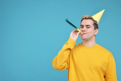 Photo of Young man with party hat and blower on light blue background, space for text