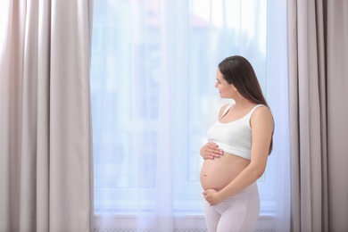 Photo of Young beautiful pregnant woman near window at home