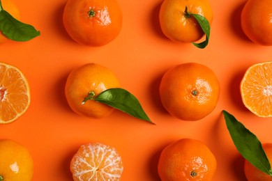 Delicious tangerines and green leaves on orange background, flat lay