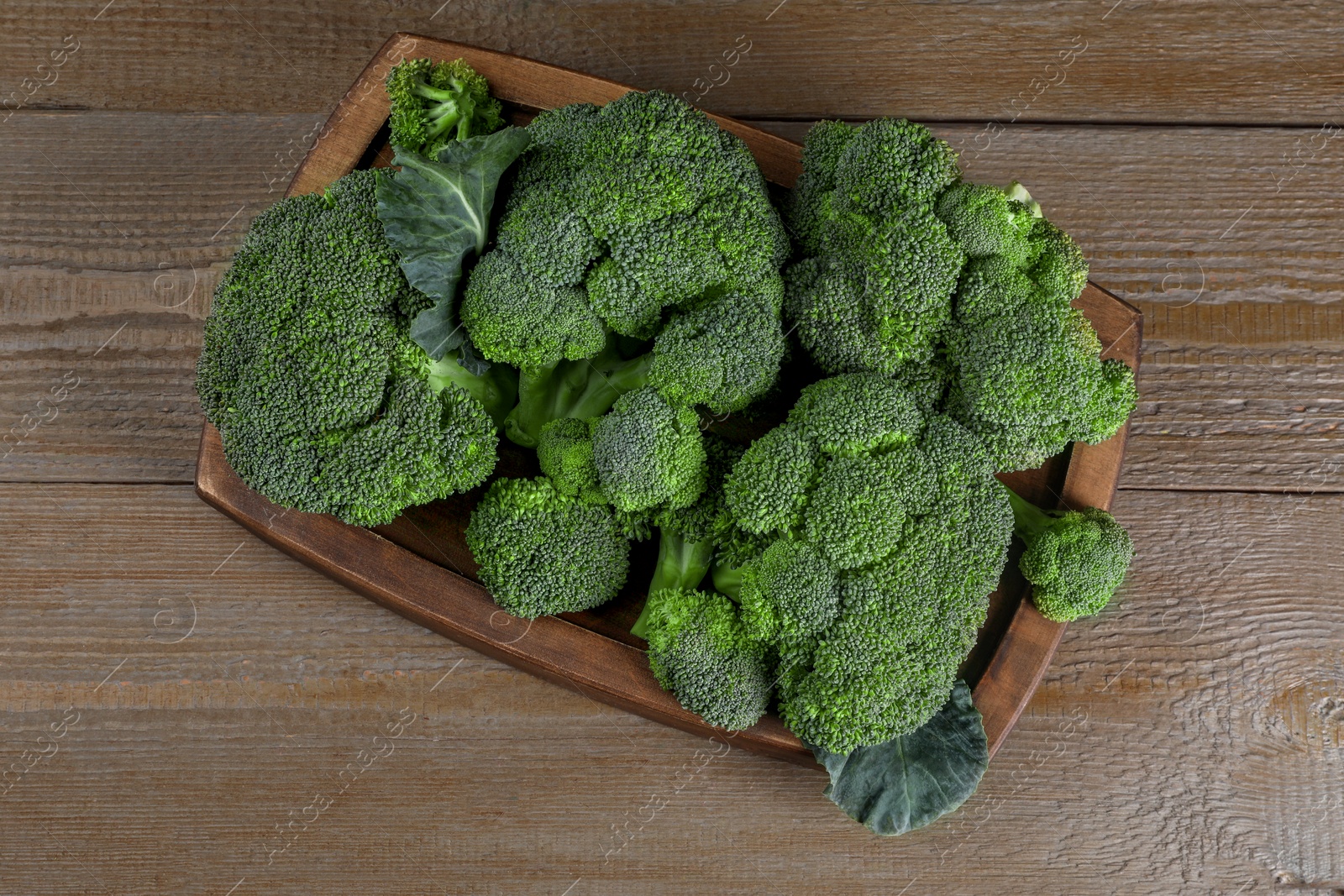 Photo of Tray with fresh raw broccoli on wooden table, top view