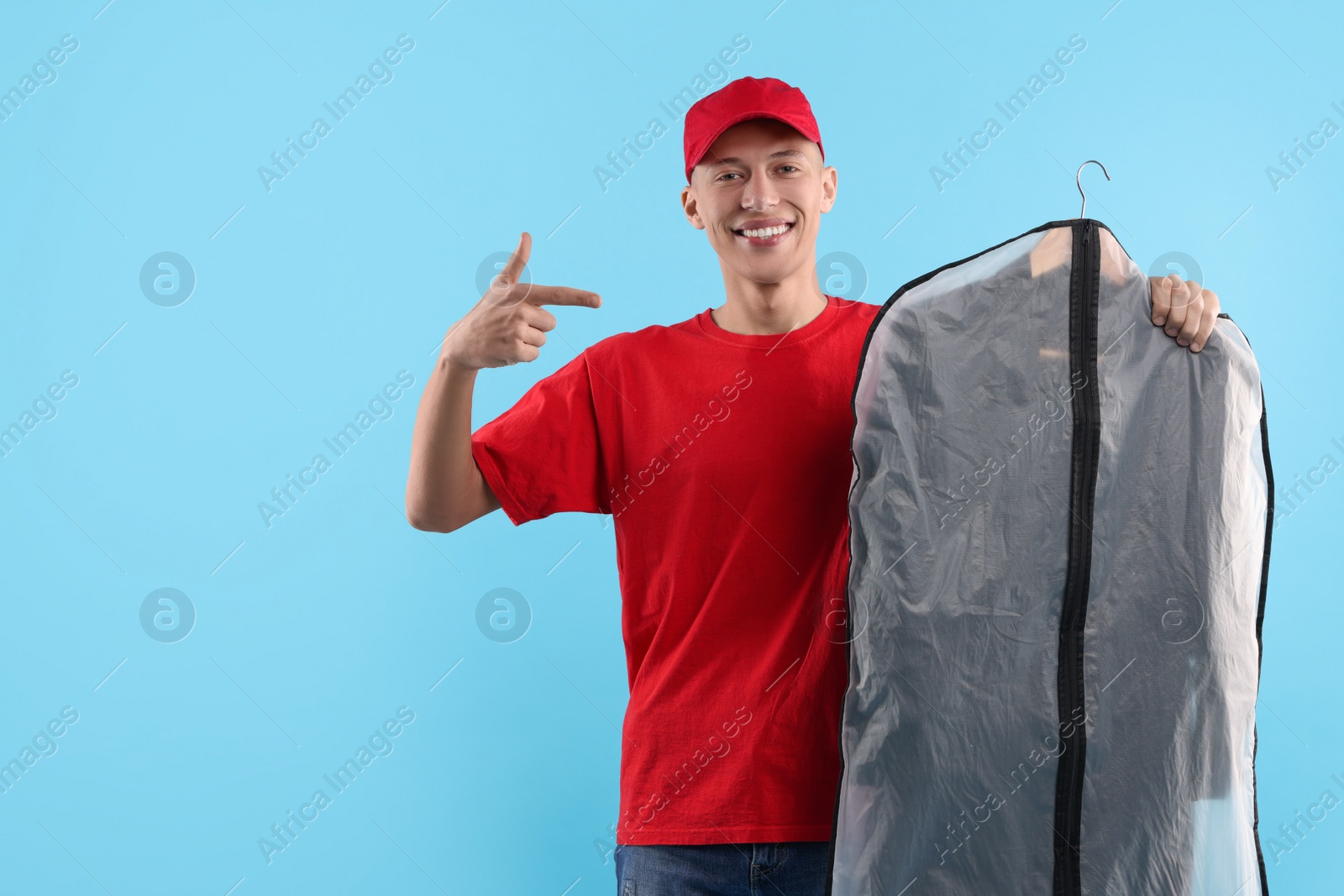 Photo of Dry-cleaning delivery. Happy courier holding garment cover with clothes on light blue background