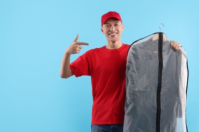 Dry-cleaning delivery. Happy courier holding garment cover with clothes on light blue background
