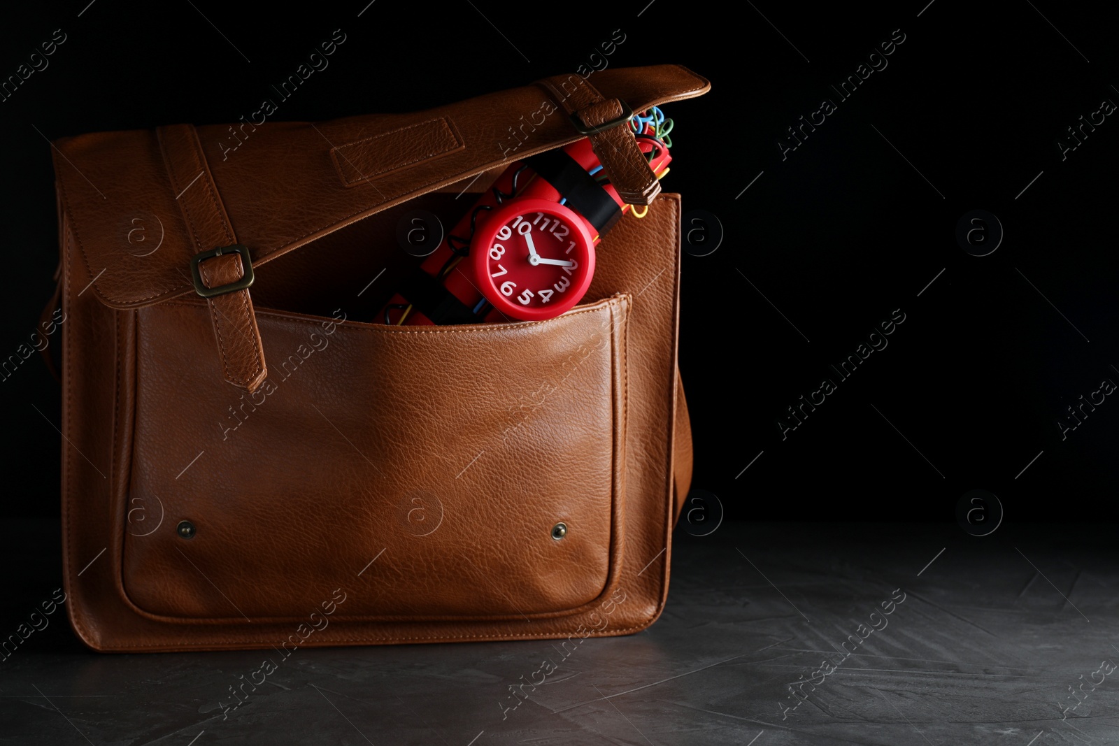 Photo of Leather briefcase with dynamite time bomb on grey table against black background. Space for text